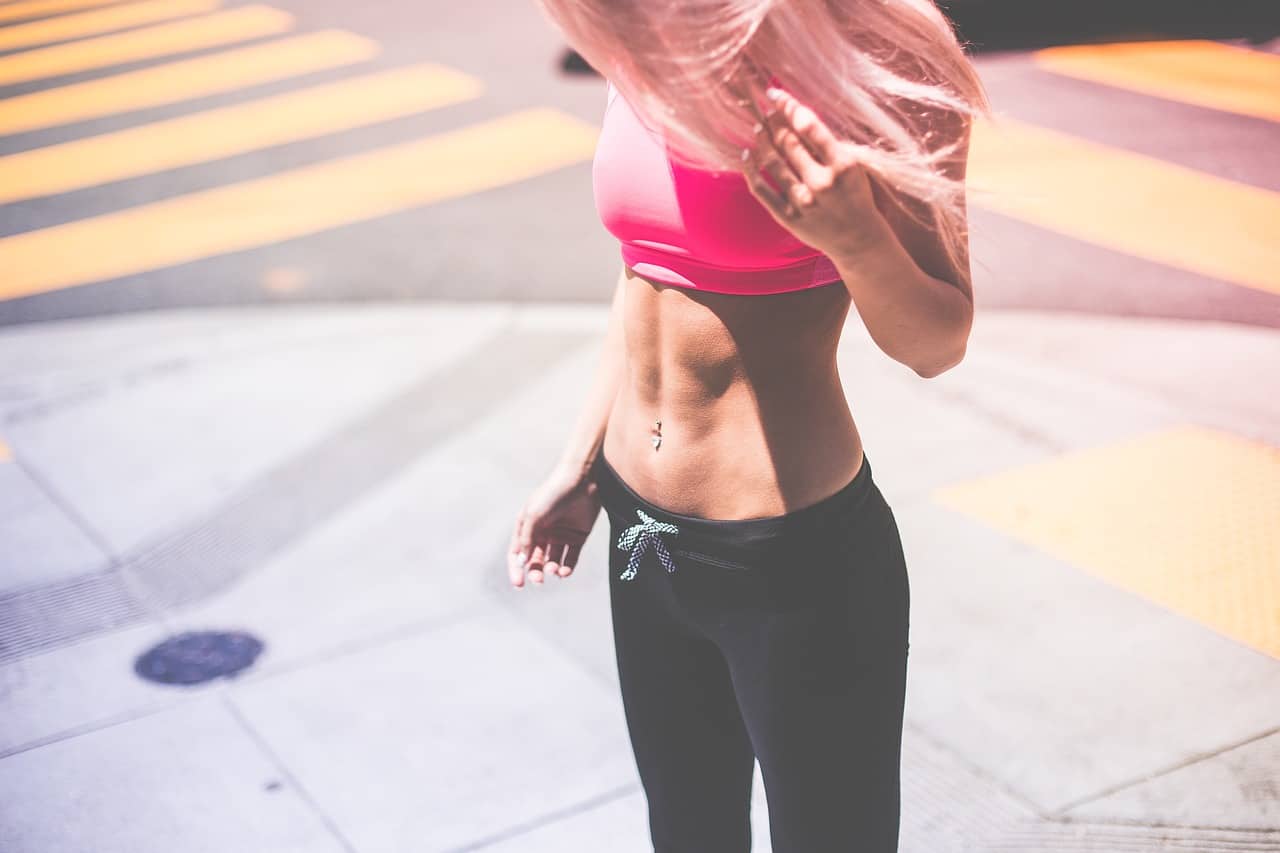 blonde-woman-wearing-pink-sports-bra-and-black-draw-string-pants-with-flat-belly